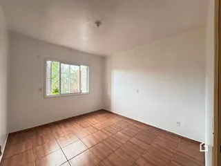 Uma sala com piso de cerâmica marrom e janela com venezianas.
