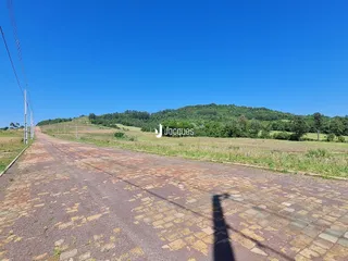 Vista da estrada de acesso rural com colinas arborizadas ao fundo.