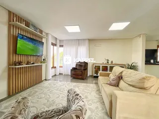 Sala de estar ampla com sofá e televisão montada em painel de madeira.