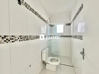Foto de um banheiro com revestimento branco e box de vidro transparente.