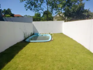 Vista de um quintal com piscina e gramado cercado por um muro branco.