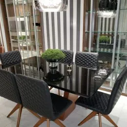 Mesa de jantar escura com cadeiras estofadas em um ambiente interno com grandes portas de vidro.