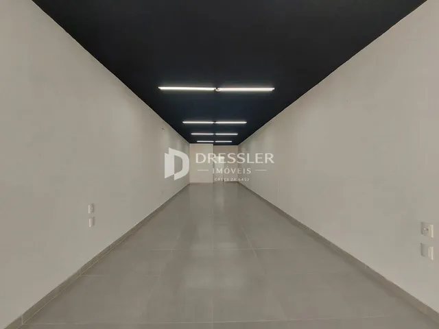 Hall de corredor longo com paredes brancas e piso claro.