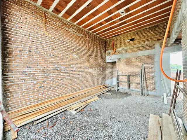 Vista interna de uma construção com paredes de tijolo aparente e teto de madeira.
