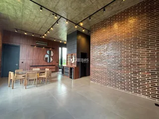 Ambiente interno de uma sala de jantar com piso de concreto e parede de tijolos aparentes.