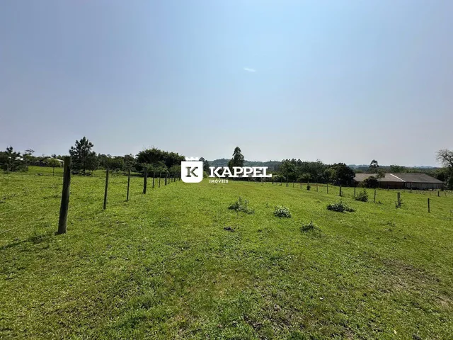 Campo gramado com cerca e árvores ao fundo.