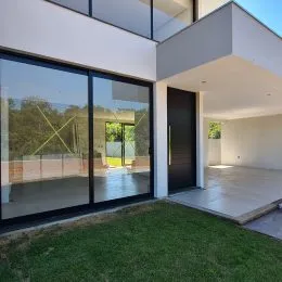 Fachada da residência com grandes portas de vidro e área externa gramada.