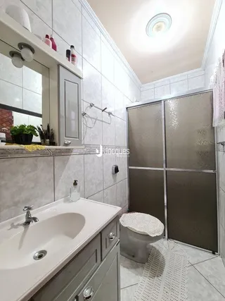 Banheiro com revestimento cerâmico e box de vidro.