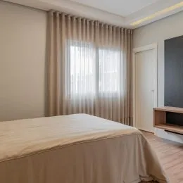 Foto de um quarto com cama e cortinas claras.