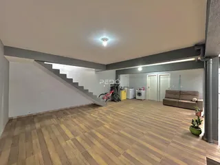 Sala de estar com piso de madeira e escadaria visível.