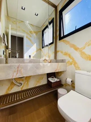 O interior de um banheiro apresenta revestimento em tons de mármore e detalhes em dourado.