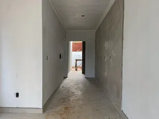 Corredor longo e estreito com paredes brancas e piso de concreto.
