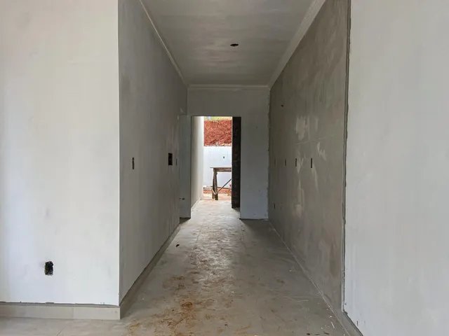 Corredor longo e estreito com paredes brancas e piso de concreto.