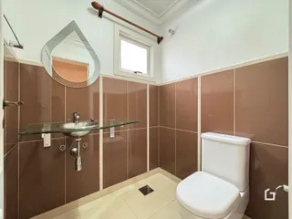 Banheiro com revestimento de azulejos marrons e bancada de vidro.