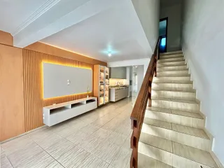 Interior de uma sala de estar com piso de cerâmica e escadaria de madeira.