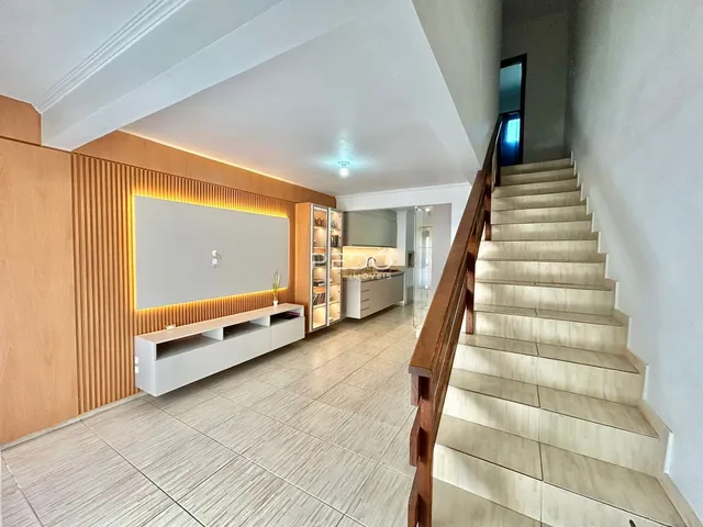 Interior de uma sala de estar com piso de cerâmica e escadaria de madeira.