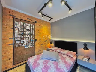 Quarto com parede de tijolos aparentes e cabeceira escura.