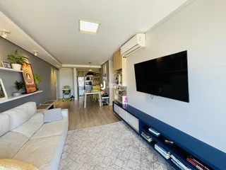 Sala de estar com sofá branco e televisão em um apartamento em Lajeado.