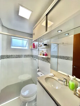 Interior de um banheiro moderno com box de vidro e louças brancas.