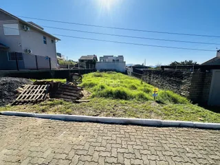 Vista externa de uma propriedade com muro de alvenaria e área gramada.