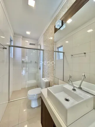 Banheiro com box de vidro e louças brancas em um imóvel.