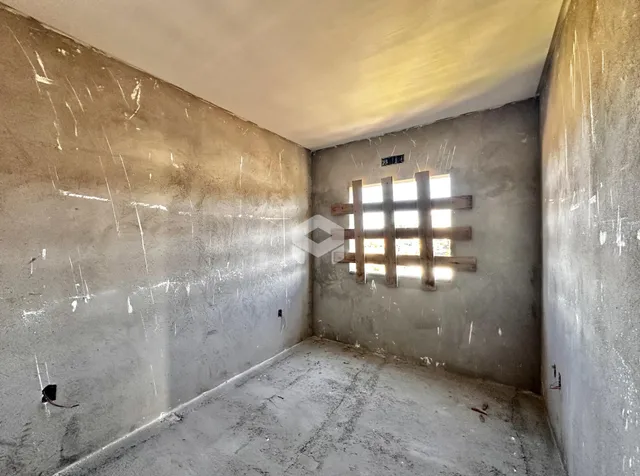 Interior de um espaço com paredes de concreto aparente e piso cru.