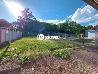 Vista externa de um terreno com grama e vegetação sob um céu azul.