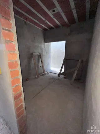 Interior de um cômodo com paredes de alvenaria exposta e piso cru.