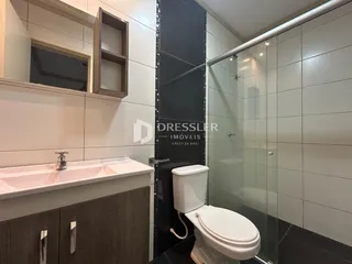 Interior de um banheiro com revestimento cerâmico e box de vidro.