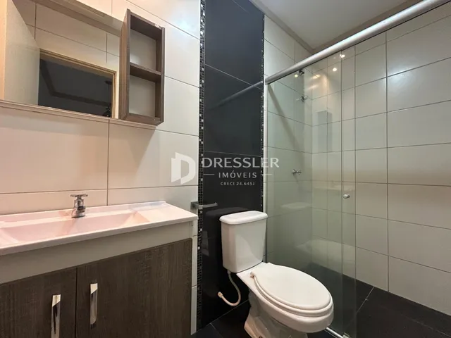 Interior de um banheiro com revestimento cerâmico e box de vidro.