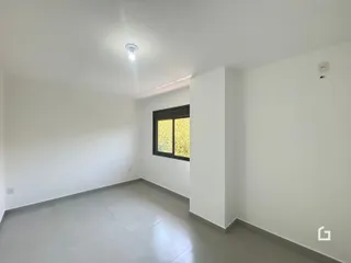 Interior de uma sala ampla com paredes brancas e piso claro.