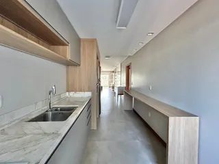 Vista interna de uma cozinha moderna com bancada de mármore e armários de madeira clara.