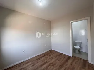 Uma sala de estar com piso de madeira clara e parede branca.