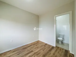 Ambiente interno de uma sala com piso de madeira clara e parede branca.