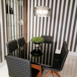 Mesa de jantar escura com cadeiras escuras em um ambiente com parede listrada.