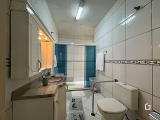 Foto de um banheiro com revestimento cerâmico branco e armários brancos.