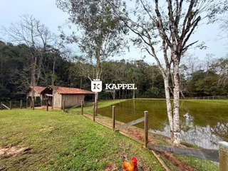 Vista externa de uma propriedade com um lago e vegetação ao fundo.