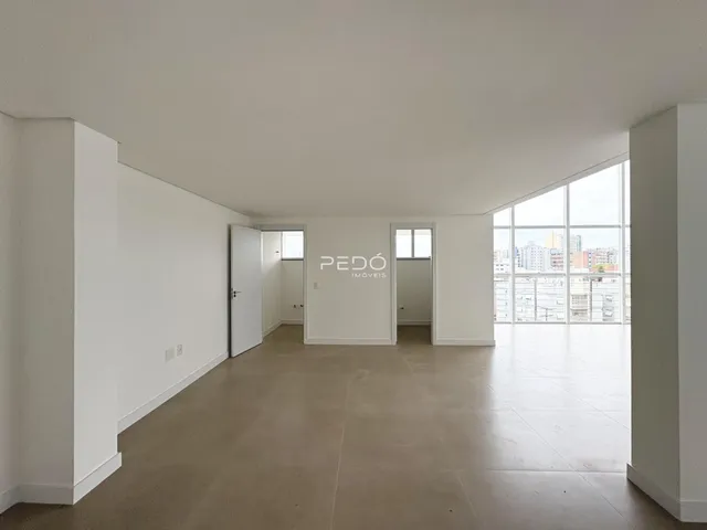 Ambiente interno de uma sala ampla com piso claro e grande janela.