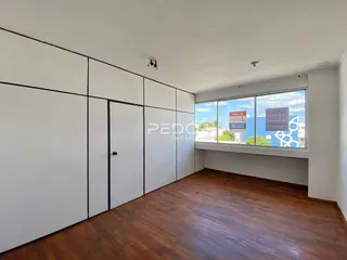 Interior de uma sala com piso de madeira e grandes janelas.