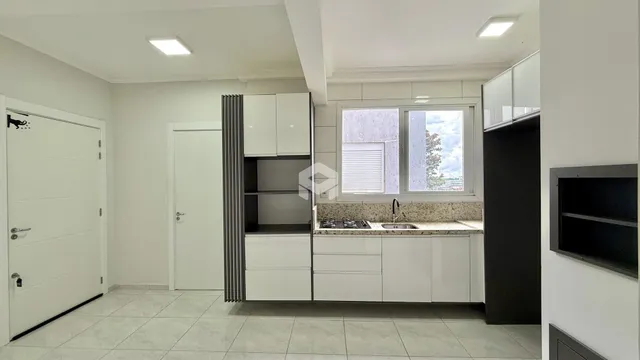 Vista interna de uma cozinha moderna com armários brancos e piso claro.