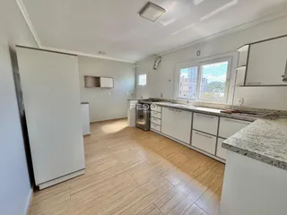 Cozinha moderna com armários brancos e piso de madeira clara.