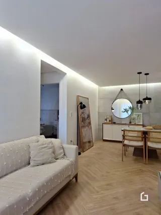 Uma sala de estar clara com sofá branco e piso de madeira.