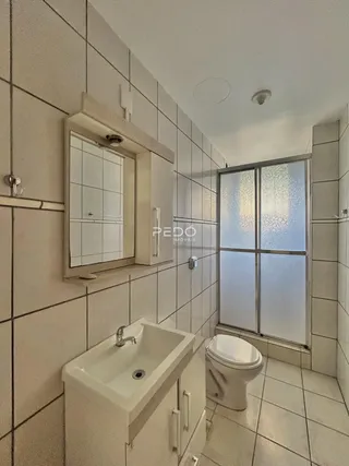 Foto de um banheiro com revestimento cerâmico e louças sanitárias brancas.