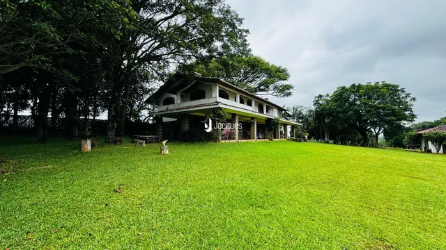 Fachada de uma casa com grande gramado e vegetação ao redor.