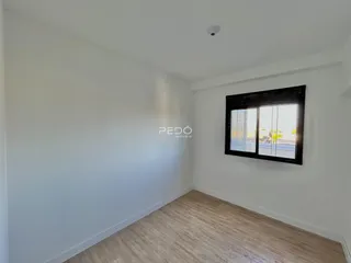 Ambiente interno de uma sala com paredes brancas e piso de madeira clara.