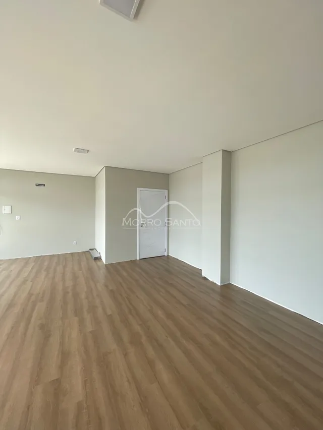 Vista interna de um ambiente amplo com piso de madeira clara e paredes brancas.