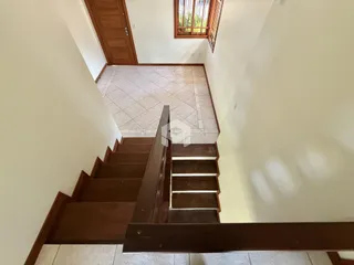 Vista do corredor com escadas de madeira e piso de cerâmica.