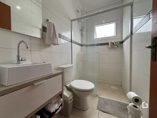 Banheiro com revestimento cerâmico branco e box de vidro.