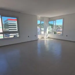 Vista interna de um ambiente amplo com piso claro e grandes janelas.