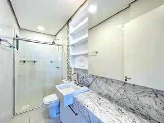 Banheiro moderno com box de vidro e bancada de mármore.